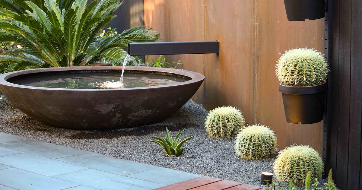Modern courtyard with circular black water bowl, corten steel spout, and vertical cactus planters in Brighton East