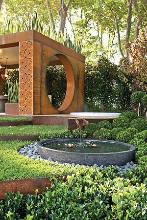 Circular water feature with corten steel moon gate structure in landscaped garden setting
