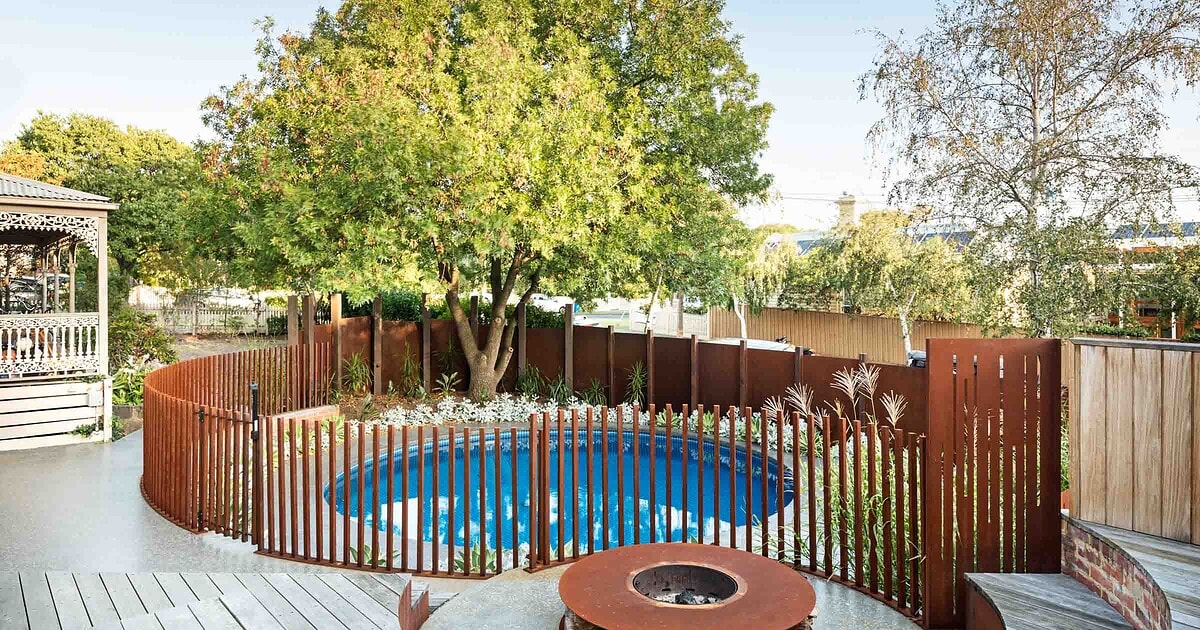 Circular blue pool surrounded by curved corten steel slat fencing, timber decking and central fire pit in Hawthorn backyard