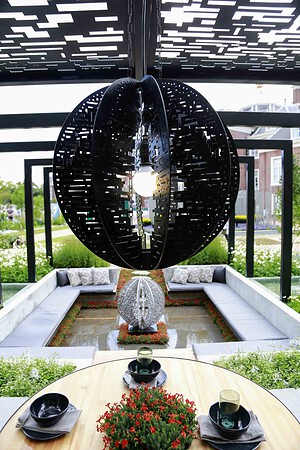 Black perforated circular moon gate sculpture suspended above sunken seating area at Mandala Garden, Nagasaki Japan