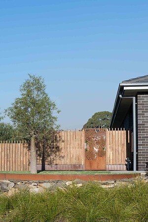 Custom corten steel gate with perforated tree pattern set in timber picket fence at Buninyong residence corner block