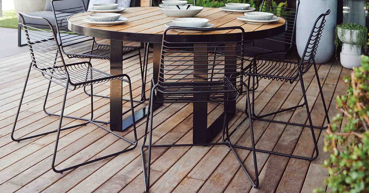 Round blackbutt timber dining table with black metal chairs on timber deck terrace overlooking St Kilda