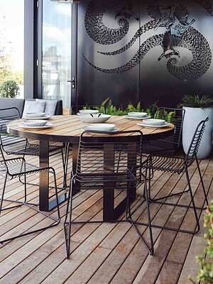 Round blackbutt timber dining table with black metal chairs on timber deck terrace overlooking St Kilda