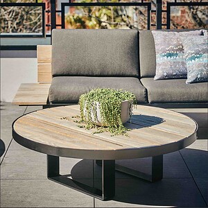 Round timber coffee table with trailing plant centerpiece on modern grey outdoor lounge setting, St Kilda rooftop