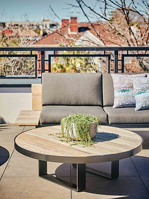 Round timber coffee table with trailing plant centerpiece on modern rooftop terrace overlooking St Kilda rooftops