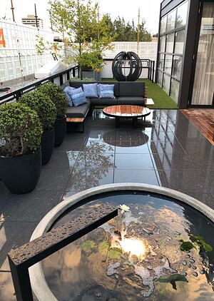 Circular water feature with fountain on wet bluestone terrace, outdoor lounge seating and artificial turf in St Kilda