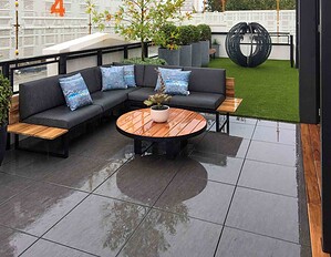 Modern corner outdoor lounge with grey cushions and blue pillows on rooftop terrace with artificial turf in St Kilda