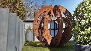 Large perforated Corten steel sculptural sphere on artificial turf rooftop terrace with modern house in St Kilda