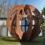 Large perforated corten steel sculptural sphere on artificial turf rooftop terrace in St Kilda