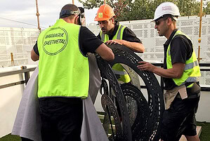 Three construction workers in high-vis vests installing black perforated steel privacy screens on St Kilda rooftop terrace