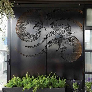 Decorative metal screening with dragon and bird motifs on black doors, green plants below, St Kilda terrace