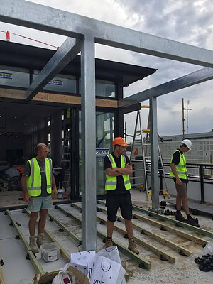 Construction workers in hi-vis installing steel frame structure on St Kilda rooftop terrace building site