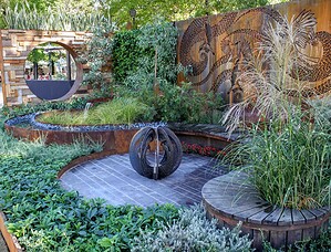 Black sculptural fire feature on stone paving with curved timber seating and native plantings in award-winning Nagasaki garden
