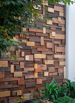 Mixed timber block feature wall with varied wood tones and textures surrounded by green foliage in Ballarat garden