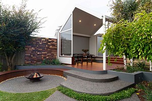 Modern outdoor dining pavilion with curved concrete seating, central fire pit and timber decking in Ballarat backyard