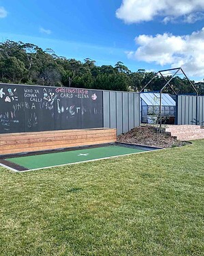 Curved exposed aggregate paths connecting lawn areas with greenhouse and chalkboard wall in Gisborne country garden