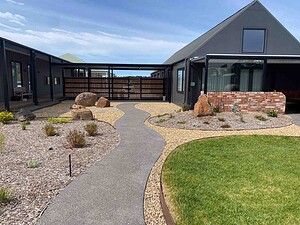 Curved exposed aggregate paths wind through landscaped courtyard with basalt boulders and native plants in Gisborne