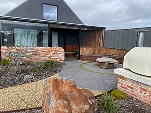 Curved exposed aggregate paths wind through contemporary garden with brick walls and native plantings in Gisborne