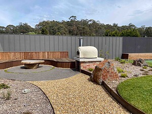 Outdoor pizza oven with chimney on brick base, timber seating and exposed aggregate paths in Gisborne garden