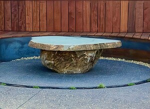 Round natural stone water feature with flowing water positioned on exposed aggregate paving in Gisborne country garden