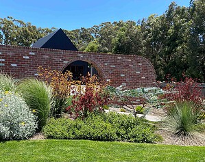 Curved brick wall with arched moon gate opening framed by native plantings and ornamental grasses in Buninyong garden