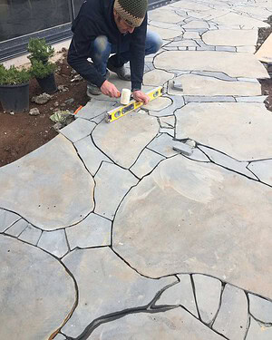 Worker installing irregular flagstone paving with spirit level at Mount Buninyong country estate garden project