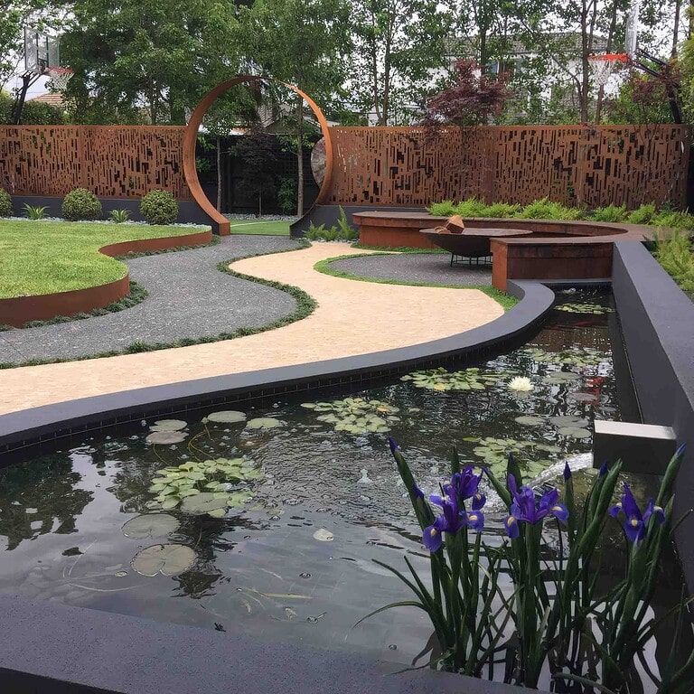Contemporary water feature with lily pond, circular corten steel moon gate entry, curved pathways and purple iris plantings