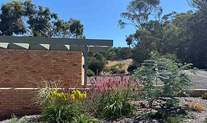 Modern brick pavilion with steel pergola frame surrounded by colorful native plantings and gravel pathways