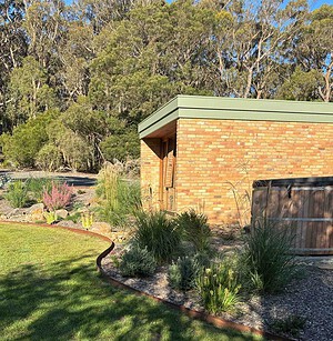 Modern brick home with curved native garden beds featuring ornamental grasses and drought-tolerant plants in regional Victoria