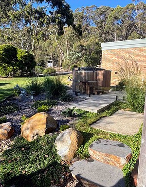 Large natural stone boulders embedded in landscaped garden with native grasses, concrete pathways, and brick wall background