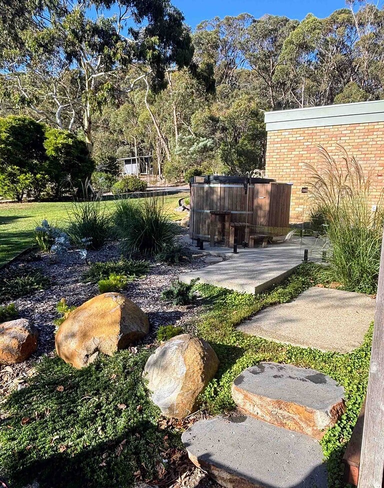 Large natural stone boulders embedded in landscaped garden with native grasses, concrete pathways, and brick wall background